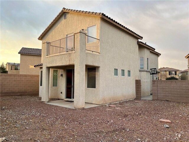 back house at dusk featuring a patio and a balcony