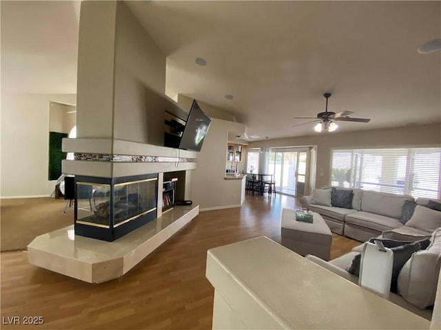 living room featuring a multi sided fireplace, wood-type flooring, and ceiling fan