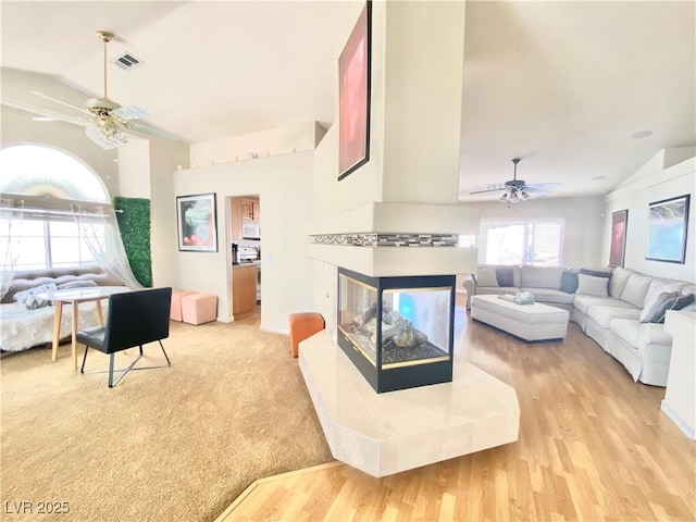 living room with ceiling fan, a multi sided fireplace, lofted ceiling, and light wood-type flooring