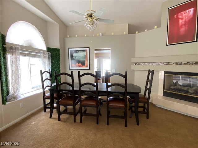 carpeted dining room with a healthy amount of sunlight, a multi sided fireplace, lofted ceiling, and ceiling fan