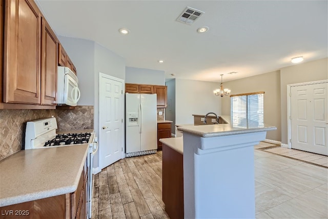 kitchen featuring decorative light fixtures, backsplash, a notable chandelier, a center island with sink, and white appliances