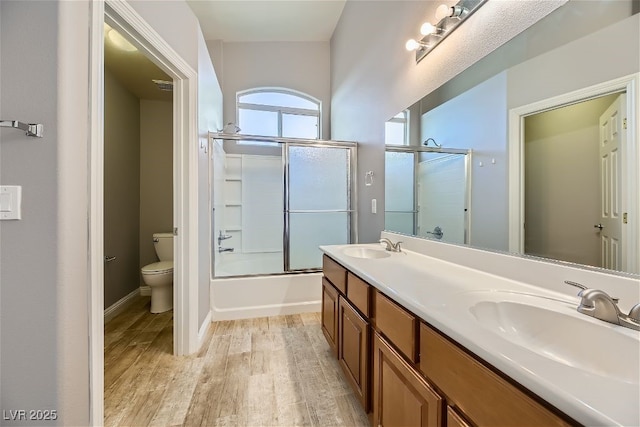 full bathroom with vanity, wood-type flooring, shower / bath combination with glass door, and toilet