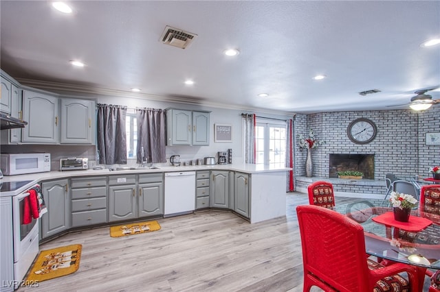 kitchen featuring gray cabinets, kitchen peninsula, a brick fireplace, white appliances, and light hardwood / wood-style flooring