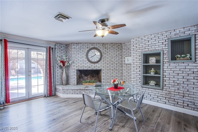 dining space featuring brick wall, hardwood / wood-style floors, ceiling fan, a brick fireplace, and french doors