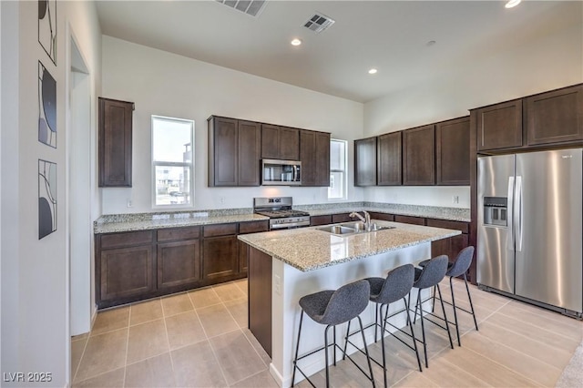 kitchen with appliances with stainless steel finishes, a breakfast bar, sink, light stone counters, and a center island with sink