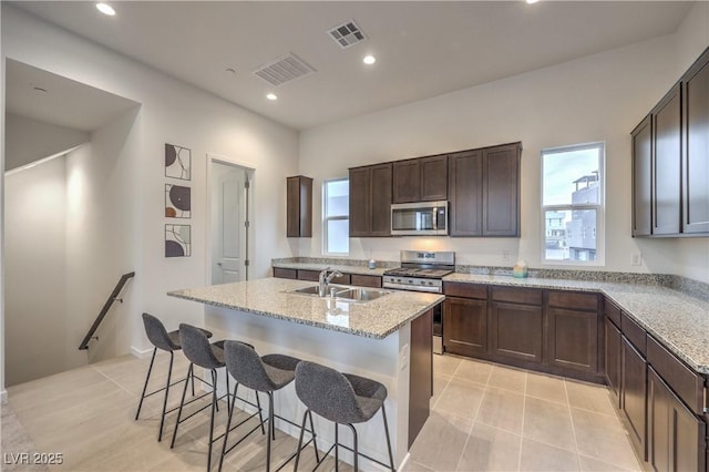 kitchen featuring light stone counters, sink, a center island with sink, and appliances with stainless steel finishes