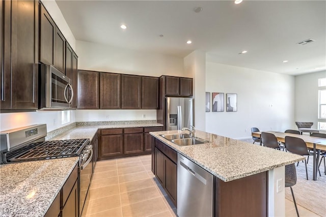 kitchen featuring sink, light tile patterned floors, a kitchen island with sink, stainless steel appliances, and light stone counters