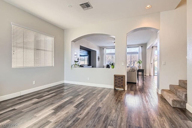 unfurnished living room featuring arched walkways, dark wood-style flooring, visible vents, and baseboards