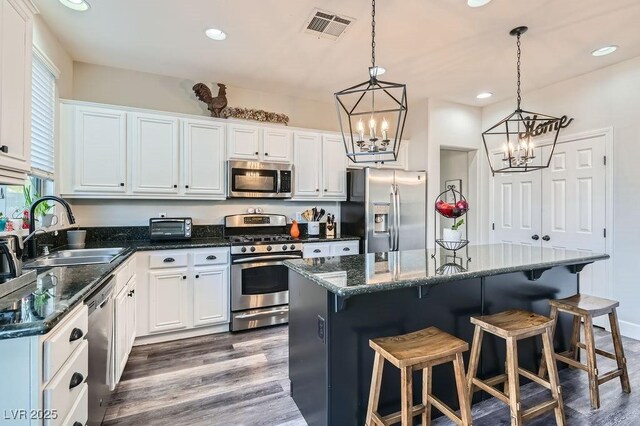 kitchen with a kitchen island, appliances with stainless steel finishes, decorative light fixtures, sink, and white cabinets