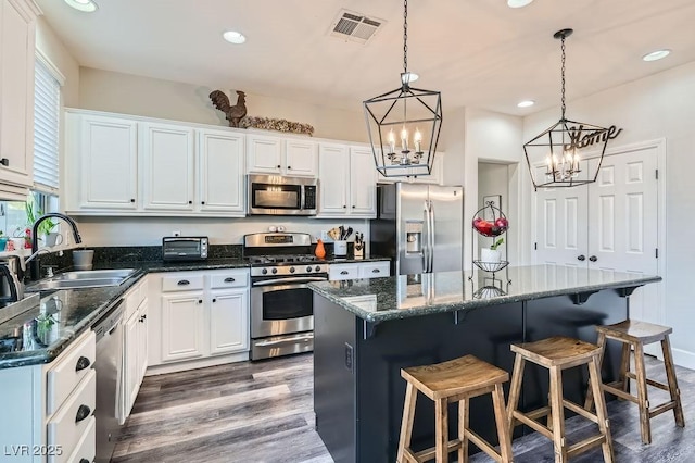 kitchen with visible vents, white cabinets, appliances with stainless steel finishes, a center island, and a sink