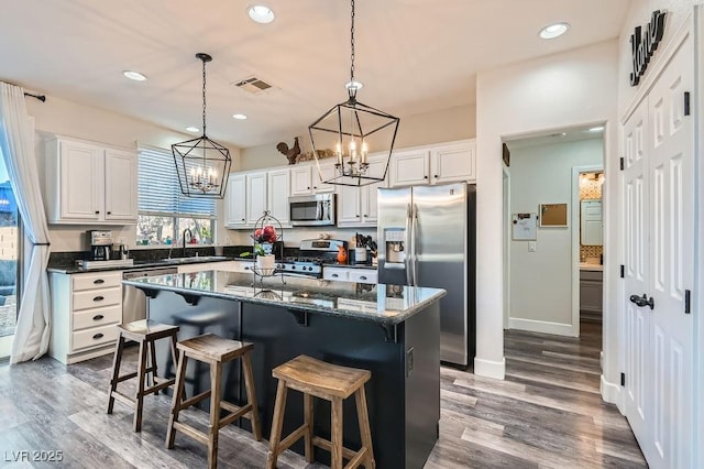 kitchen with a sink, a kitchen island, visible vents, white cabinets, and appliances with stainless steel finishes