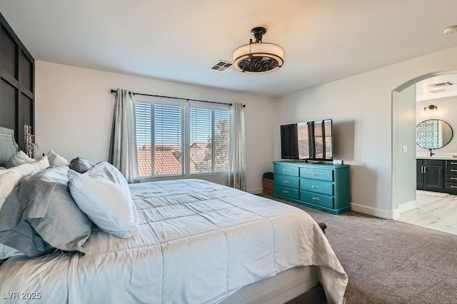 bedroom with arched walkways, baseboards, visible vents, and light colored carpet