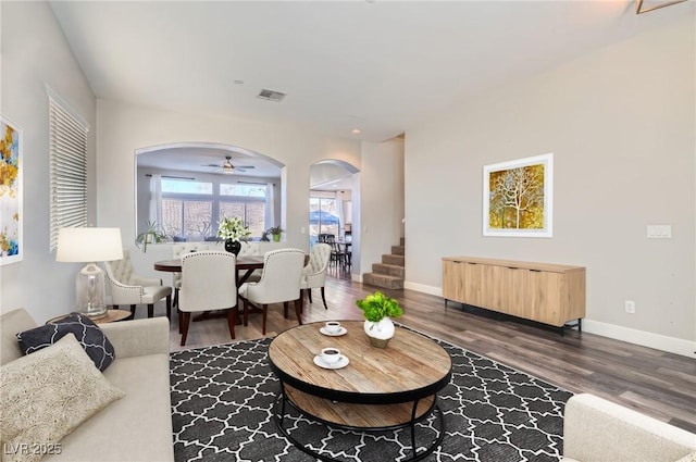 living area with arched walkways, visible vents, dark wood finished floors, and baseboards