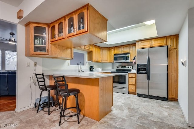 kitchen featuring stainless steel appliances, kitchen peninsula, ceiling fan, and a kitchen bar