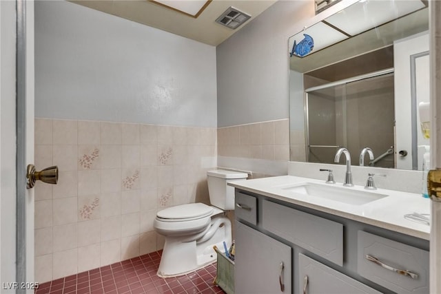 bathroom featuring tile patterned floors, toilet, tile walls, vanity, and a shower with door