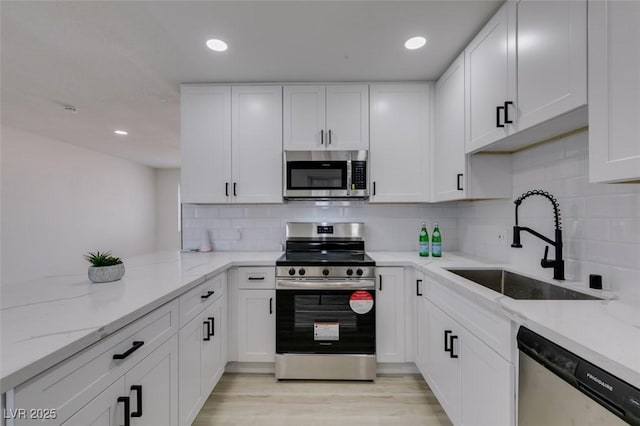 kitchen with stainless steel appliances, white cabinetry, light stone countertops, and sink