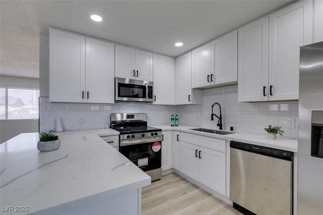 kitchen with sink, light stone counters, appliances with stainless steel finishes, decorative backsplash, and white cabinets