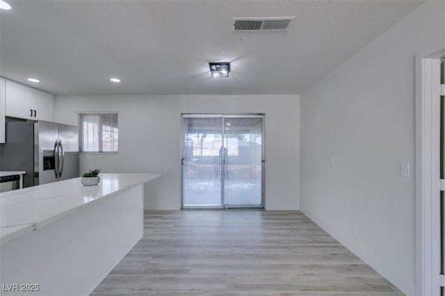 kitchen featuring white cabinets, light stone countertops, stainless steel fridge, and light hardwood / wood-style floors