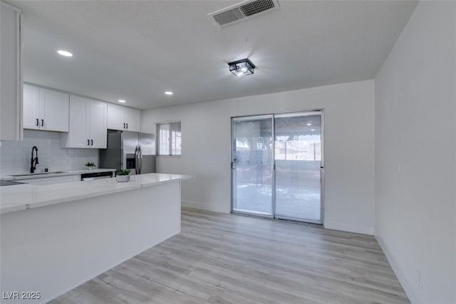 kitchen with sink, white cabinets, backsplash, stainless steel fridge with ice dispenser, and light stone countertops