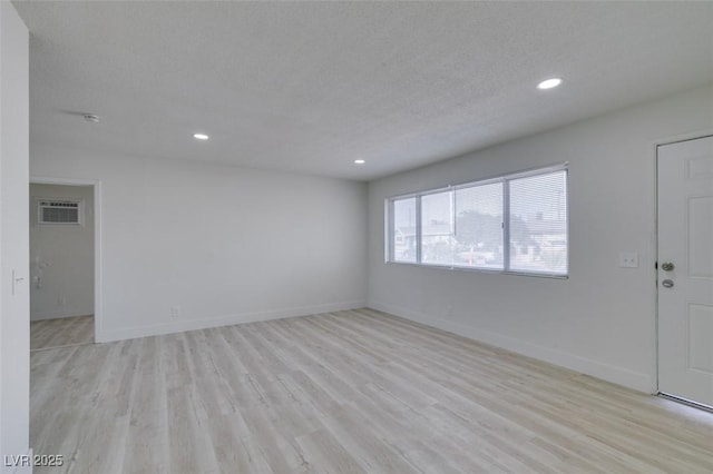 spare room featuring a wall mounted air conditioner, light hardwood / wood-style floors, and a textured ceiling