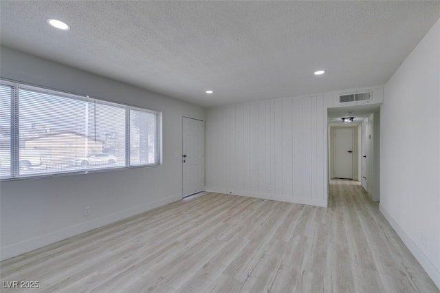 unfurnished room with wood walls, a textured ceiling, and light wood-type flooring