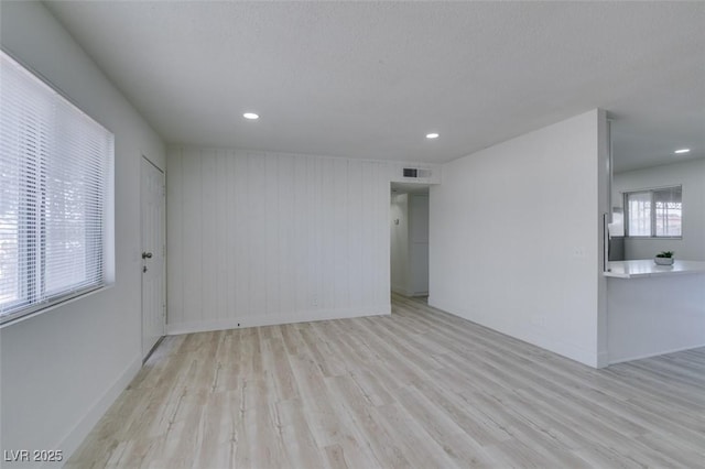 unfurnished room with light hardwood / wood-style floors, a textured ceiling, and wood walls