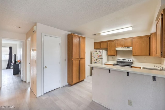 kitchen featuring a kitchen bar, sink, stainless steel range with electric stovetop, white refrigerator, and kitchen peninsula