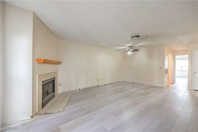 unfurnished living room with ceiling fan, light hardwood / wood-style flooring, a tile fireplace, and a textured ceiling