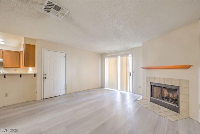 unfurnished living room featuring a fireplace, a textured ceiling, and light wood-type flooring