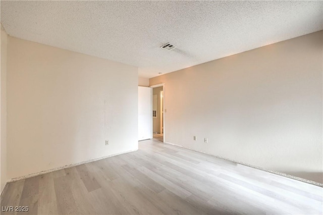 empty room with light wood-type flooring and a textured ceiling