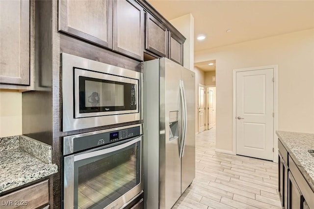 kitchen featuring stainless steel appliances, light stone countertops, dark brown cabinets, and light hardwood / wood-style flooring