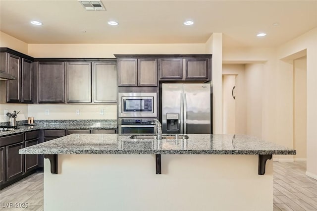 kitchen with stone counters, appliances with stainless steel finishes, sink, a kitchen bar, and dark brown cabinets