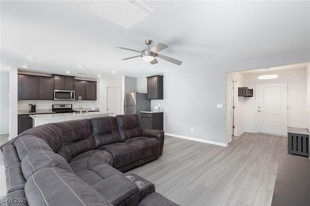 living room with ceiling fan, sink, and light wood-type flooring