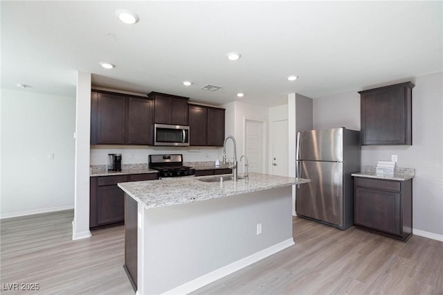 kitchen with appliances with stainless steel finishes, sink, a kitchen island with sink, dark brown cabinets, and light hardwood / wood-style flooring