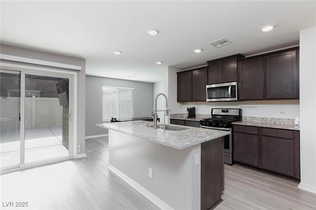 kitchen featuring appliances with stainless steel finishes, an island with sink, sink, dark brown cabinetry, and light hardwood / wood-style flooring