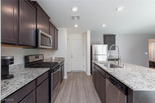 kitchen featuring sink, stainless steel appliances, light hardwood / wood-style floors, an island with sink, and light stone countertops