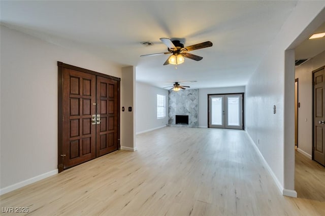 unfurnished living room with a fireplace, light hardwood / wood-style flooring, french doors, and ceiling fan