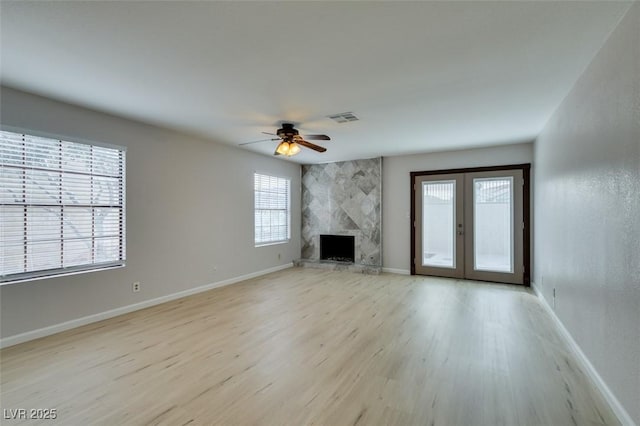 unfurnished living room with french doors, ceiling fan, a high end fireplace, and light hardwood / wood-style floors