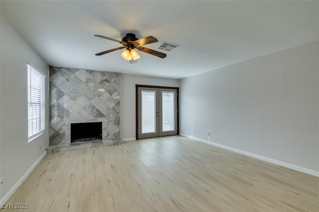 unfurnished living room with ceiling fan, light wood-type flooring, a fireplace, and french doors