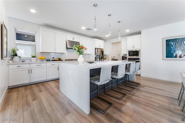 kitchen with white cabinetry, appliances with stainless steel finishes, decorative light fixtures, and a kitchen island with sink