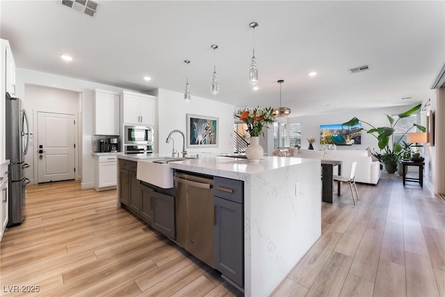 kitchen featuring hanging light fixtures, appliances with stainless steel finishes, a kitchen island with sink, and white cabinets