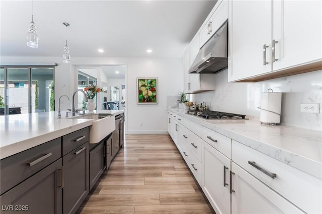 kitchen with pendant lighting, sink, light stone counters, white cabinets, and stainless steel gas stovetop