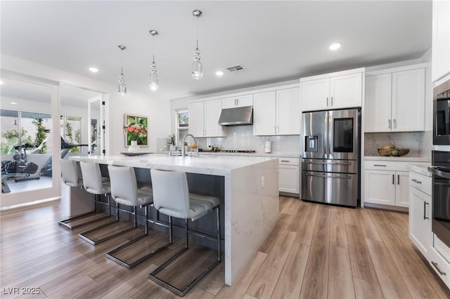 kitchen featuring stainless steel refrigerator with ice dispenser, a kitchen island with sink, white cabinets, and backsplash