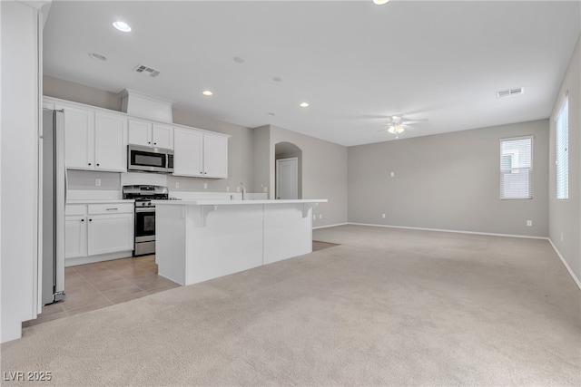 kitchen featuring light carpet, visible vents, arched walkways, appliances with stainless steel finishes, and a kitchen breakfast bar