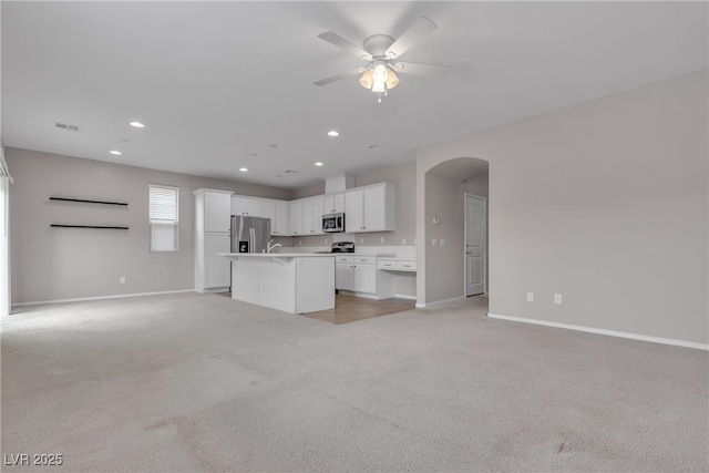 kitchen featuring arched walkways, light colored carpet, appliances with stainless steel finishes, open floor plan, and a kitchen island with sink