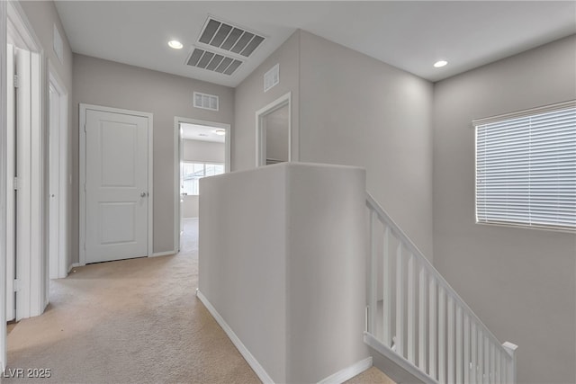 hallway with light colored carpet, baseboards, visible vents, and an upstairs landing