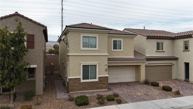 view of front of house featuring a garage, stone siding, a tiled roof, decorative driveway, and stucco siding