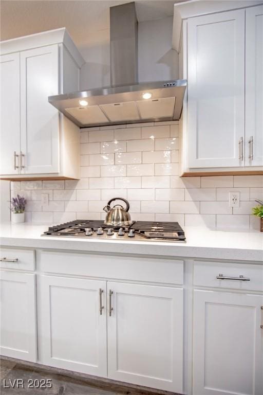 kitchen with wall chimney range hood, white cabinets, and backsplash