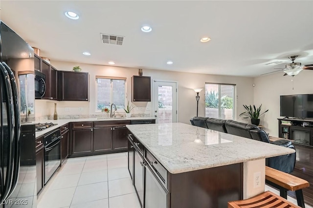 kitchen featuring dark brown cabinetry, sink, light tile patterned floors, a kitchen island, and black appliances