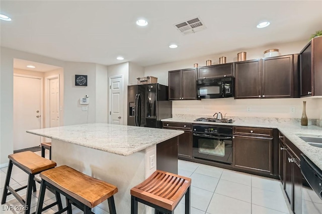 kitchen featuring light tile patterned floors, black appliances, a breakfast bar, and light stone countertops